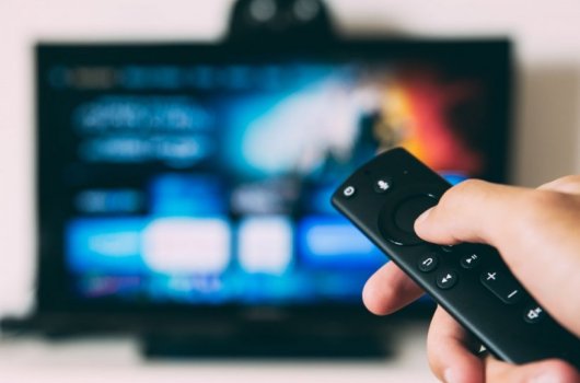 A hand is holding a remote control in front of a television