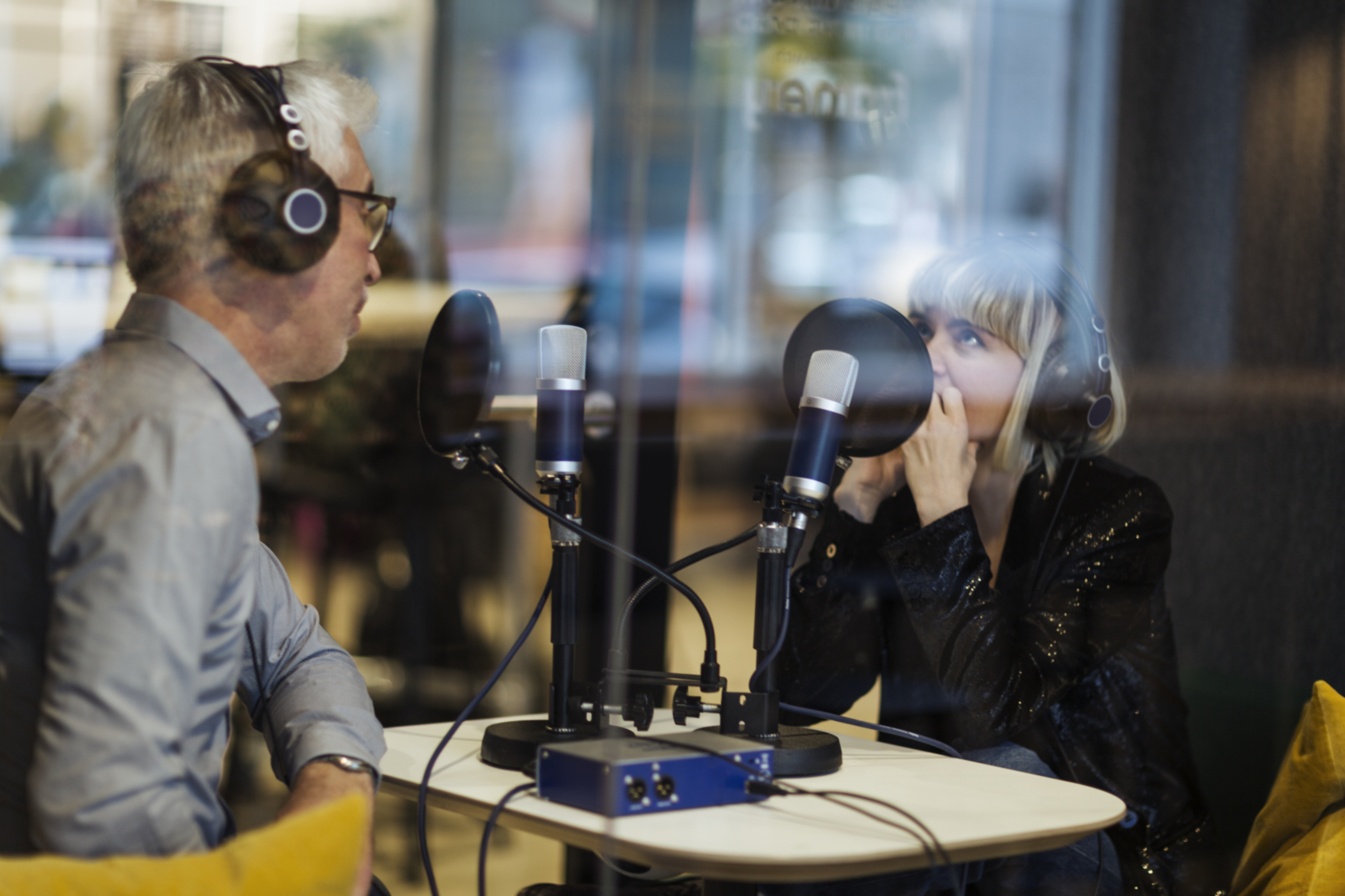 En man och en kvinna sitter med hörlurar och pratar framför mikrofoner.