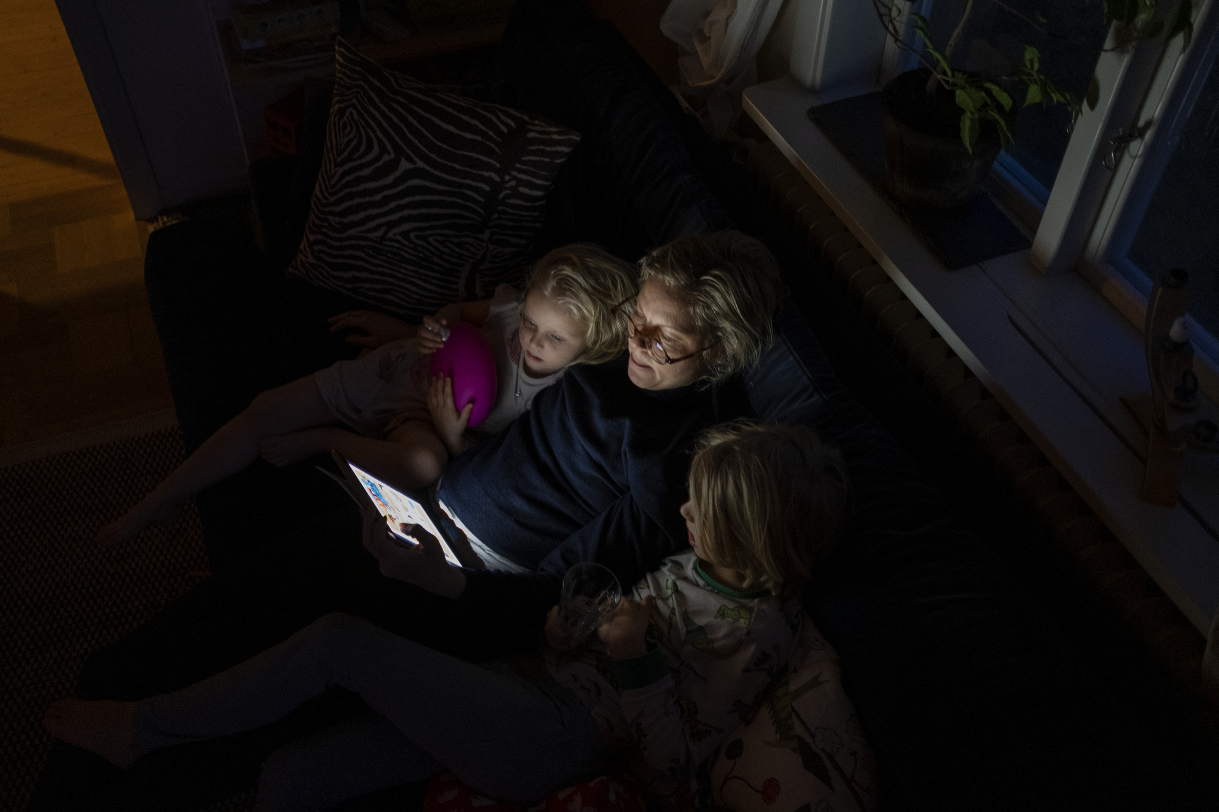 A woman reading to two children on a couch.