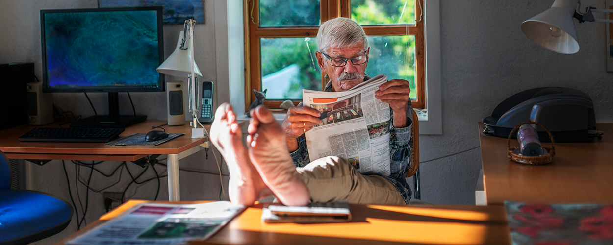 A man reading the newspaper with his feet up on the table.