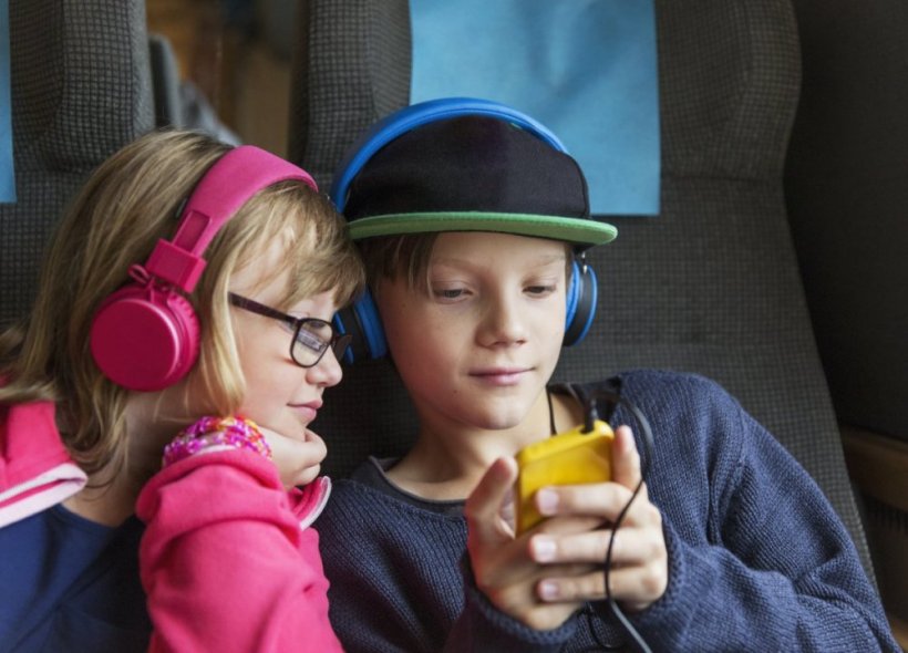 Two kids with headphones watching a cell phone