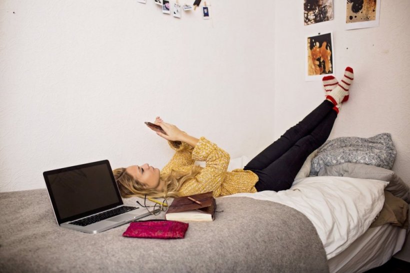 Kvinna som ligger på en säng och kollar sin mobil