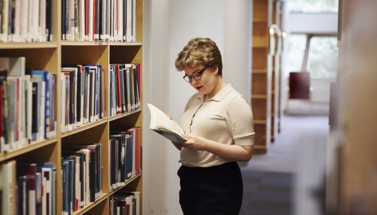 A woman reading a book in a library.