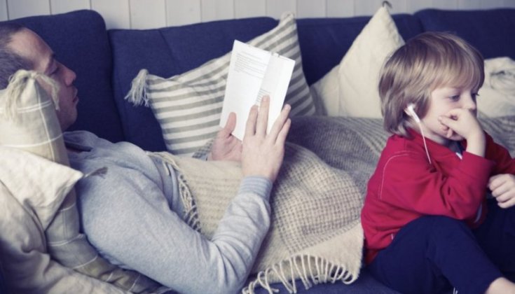  En man ligger och läser och en pojke tittar på film i en soffa